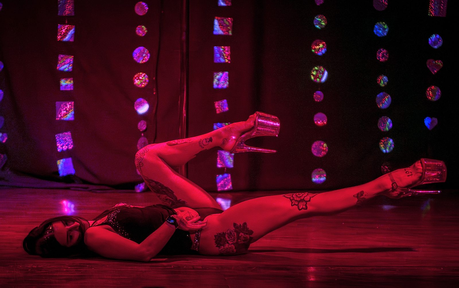 Luchi Lattero haciendo floorwork de pole exotic sobre el escenario, bajo luz roja.